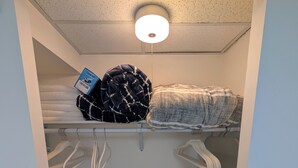 A compact storage area with a ceiling light, a folded blanket, a laundry basket, and a white crib. - Comfy 2-bedroom apartment with AC, WiFi in Oak Park (Oak Park)