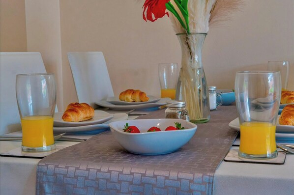 A breakfast setting with croissants, a bowl of strawberries, and glasses of orange juice on a table.