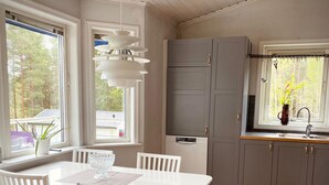 A modern kitchen with white cabinetry, a white dining table with chairs, and a window with a view of trees.