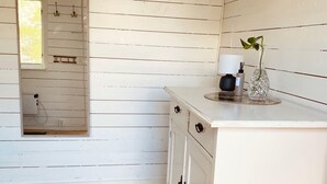 A white wooden room with a wooden floor, a white cabinet with drawers, a small window, and a vase with a plant on the cabinet.