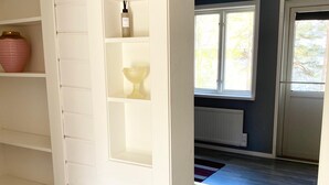 A room with white wooden shelving, a radiator, a window, and a wooden floor.