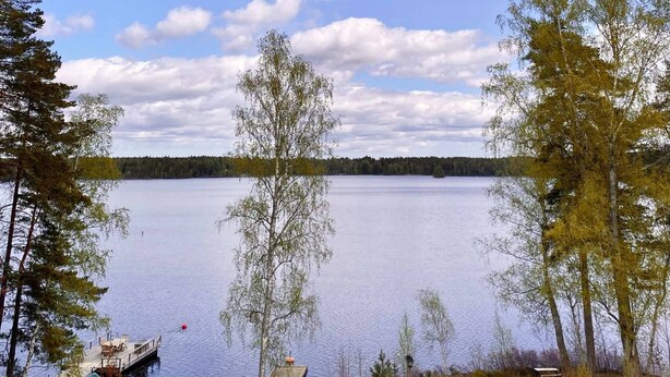 A lakeside view with a dock, a small boat, and a deck area with seating.
