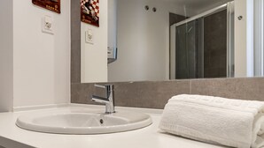 A bathroom with a white sink, a towel, and a mirror reflecting a shower. - Belem Design Studio 2 by Homing (Lisbon)