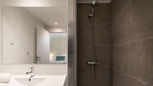 A modern bathroom with a white sink, a large mirror, and a shower with a handheld showerhead. - Belem Design Studio 1 by Homing (Lisbon)