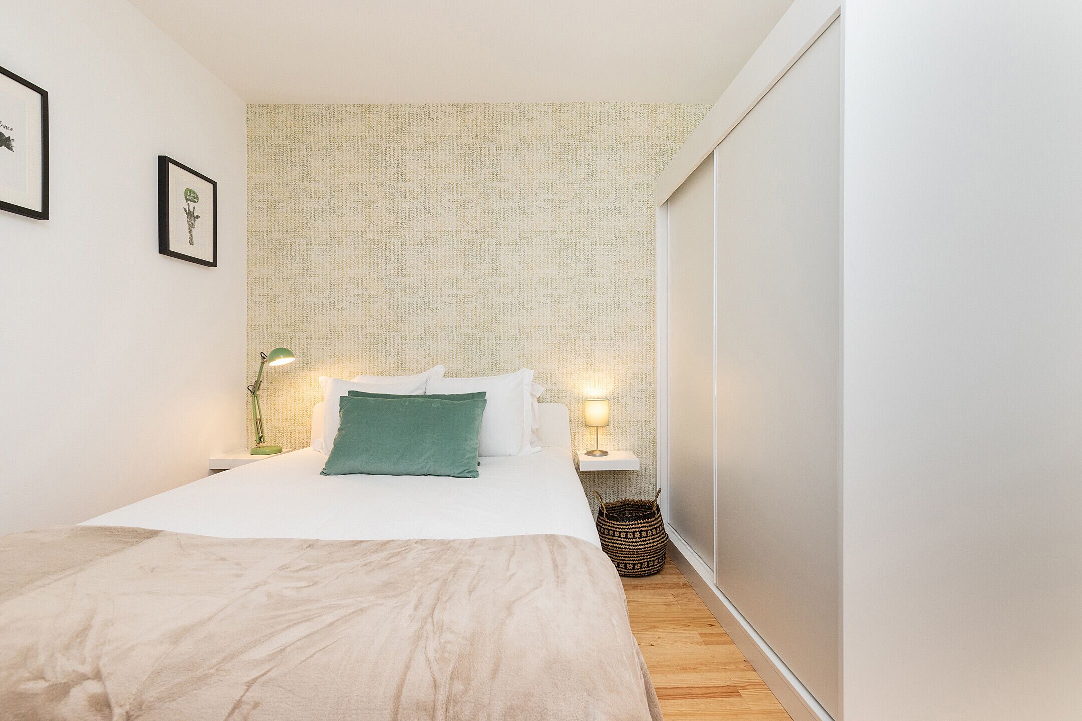 Une chambre à coucher comprenant un lit, deux tables de chevet, une lampe, un mur recouvert d’un papier peint à motifs et une armoire.