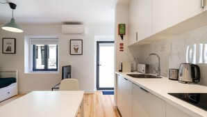 A modern kitchen with white cabinets, a sink, and a kettle. There is a window with blinds and a door leading to another room. - Belem Design Studio 1 by Homing (Lisbon)