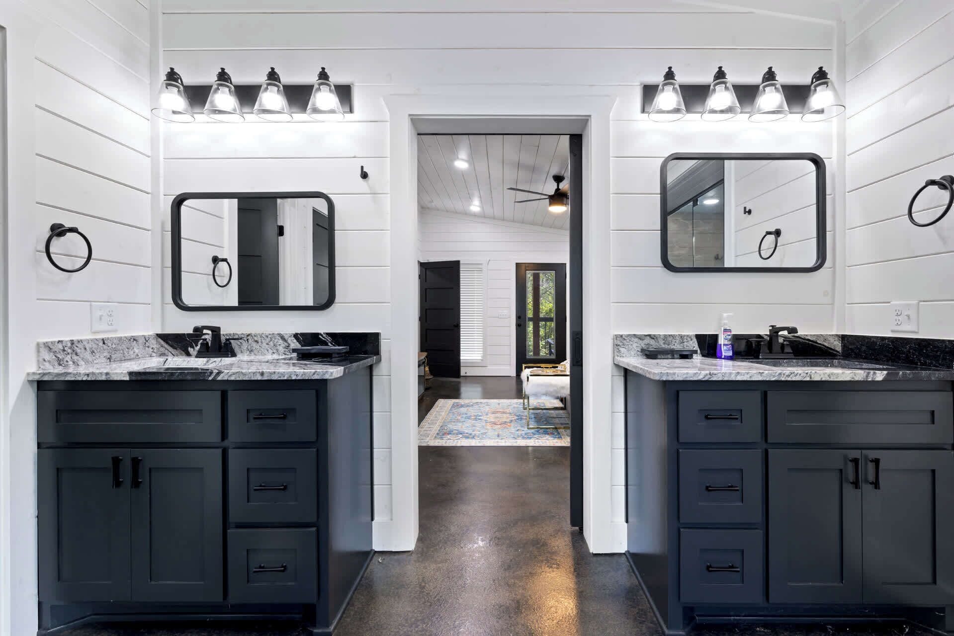 A modern bathroom with dual sinks, dark cabinets, and a central mirror.