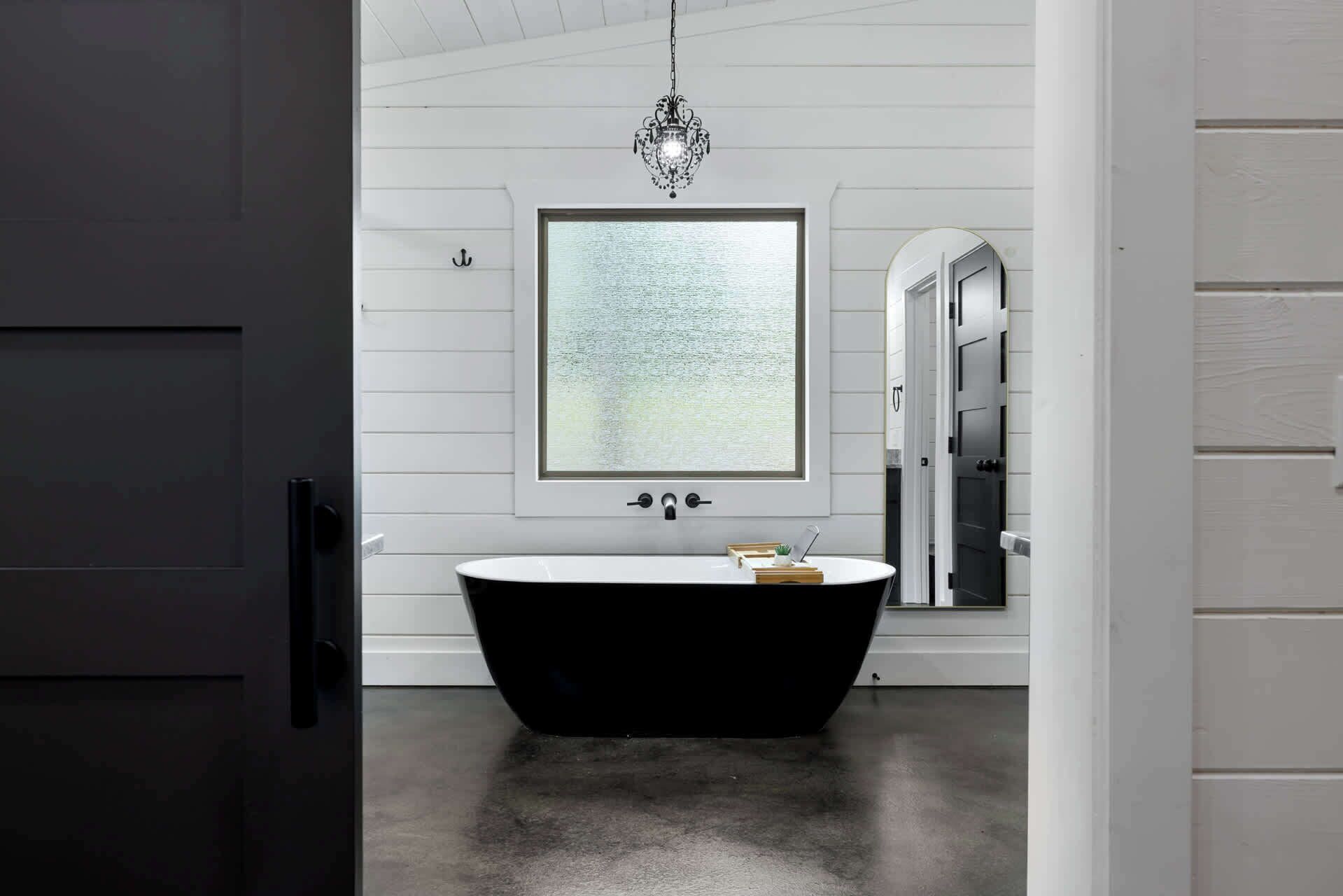 Ein modernes Badezimmer mit einer freistehenden Badewanne, einem großen Fenster mit Aussicht und einer Kandelaberleuchte.