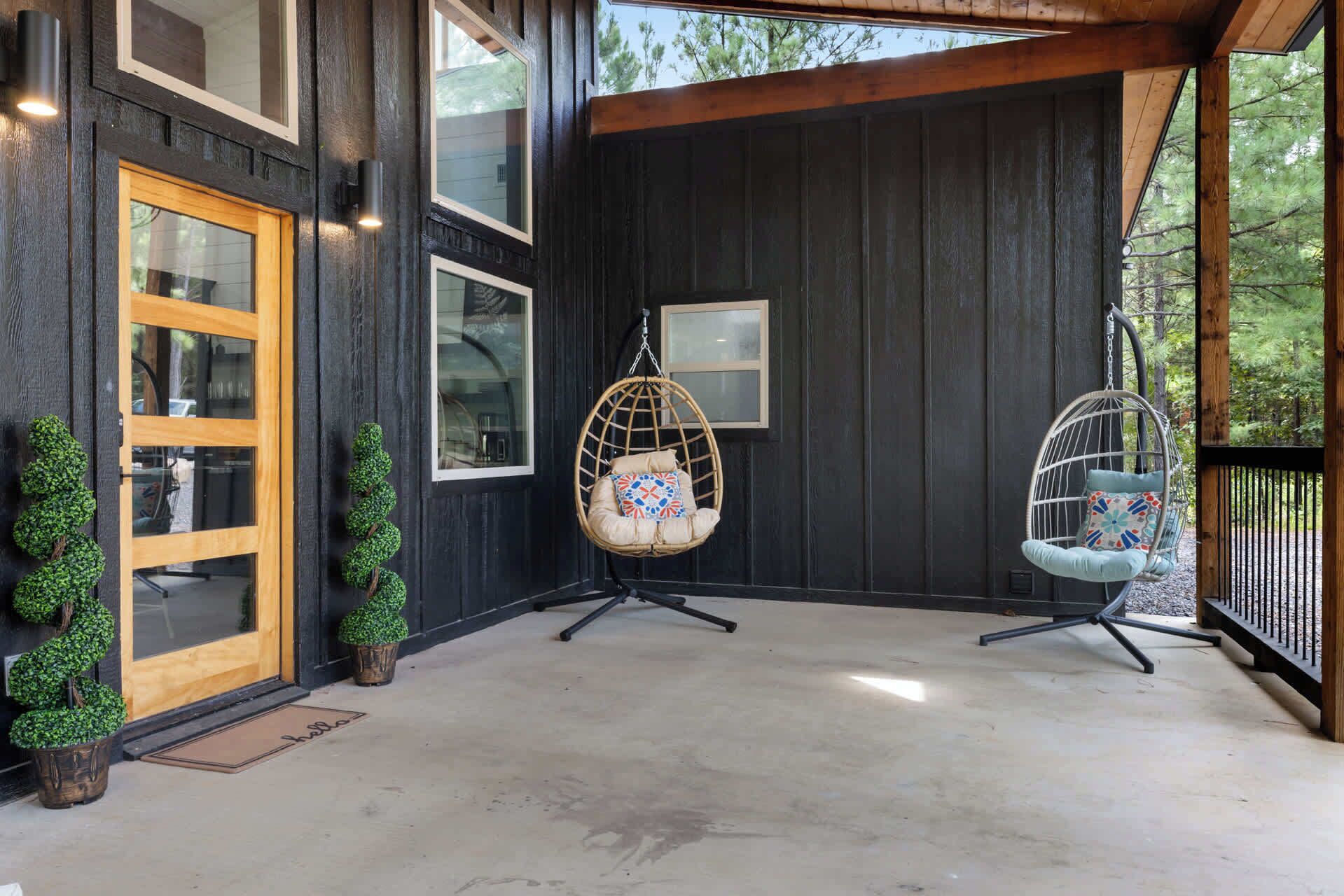 A covered porch with two hanging chairs, a wooden door, and a small potted plant.