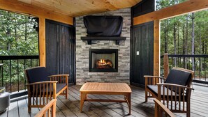 Eine Holzterrasse mit einem Kamin aus Stein, zwei Stühlen und einem Tisch.