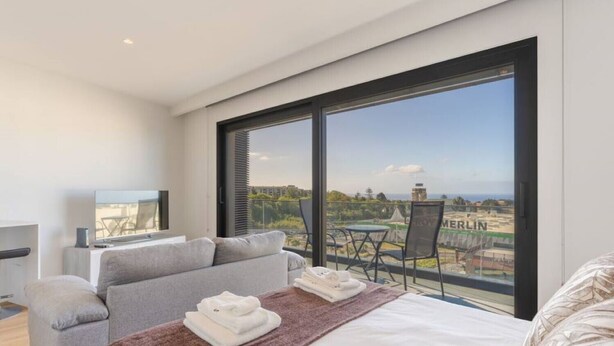 Una habitación de hotel moderna con un ventanal grande, una cama, un sofá y un televisor.