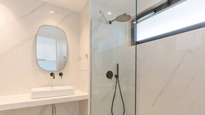 Un baño moderno con ducha de vidrio, lavamanos de mármol blanco y un espejo ovalado grande.