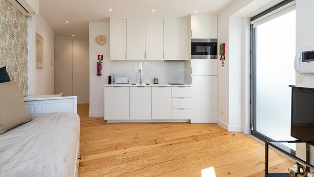Quarto moderno com cama, mesa de cabeceira pequena e janela com vista para o céu.