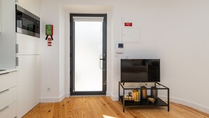 Um apartamento moderno com cozinha, uma porta que dá para uma varanda, uma televisão em um suporte e um sinal de segurança contra incêndio.