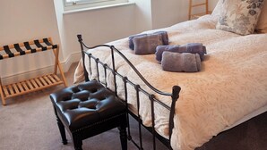 A bedroom with a bed, a window with blinds, a wooden bench, and a clothes rack. - Stylish 2-bed House in Stamford Town Centre (Stamford)