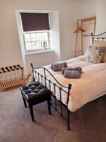 Un dormitorio con cama, una ventana con persianas, un banco de madera y un perchero.