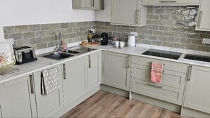 A kitchen with light grey cabinets, a stainless steel sink, and a tiled backsplash. - Stylish 2-bed House in Stamford Town Centre (Stamford)