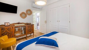 Ett sovrum med en säng, en byrå i trä, en gul stol och en tv som är monterad på väggen.