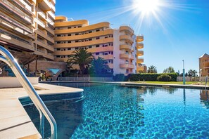 A swimming pool with clear blue water, surrounded by a modern building with multiple balconies and a brick wall. - 2 Bed-sleeps 4-vilamoura Beach-pool-spa-balcony (Loulé)
