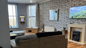 A modern living room with a stone wall, a fireplace, a television, and a sofa. - Citycenterapt-4br-wifi-freeparking-retroarcade (Newcastle-upon-Tyne)