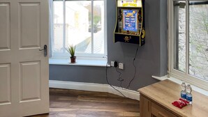 A room with a large window, a door, a small table with bottles, and a game machine. - Citycenterapt-4br-wifi-freeparking-retroarcade (Newcastle-upon-Tyne)