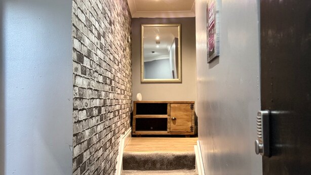 A staircase leading to a landing with a brick wall on one side and a wooden cabinet below a mirror. - Citycenterapt-4br-wifi-freeparking-retroarcade (Newcastle-upon-Tyne)