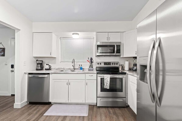 A modern kitchen with white cabinets, stainless steel appliances, and a wooden floor.