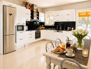 A modern kitchen with stainless steel appliances, white cabinetry, and a breakfast setup with croissants and orange juice.