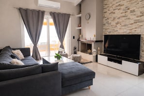 A modern living room with a grey sofa, a flat-screen TV, a fireplace, and a stone wall.