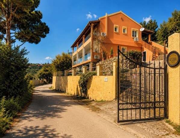 A two-story building with a gated entrance, surrounded by greenery and a clear sky. - La Casa di Kosta - Kontogialos Beach (Corfu)