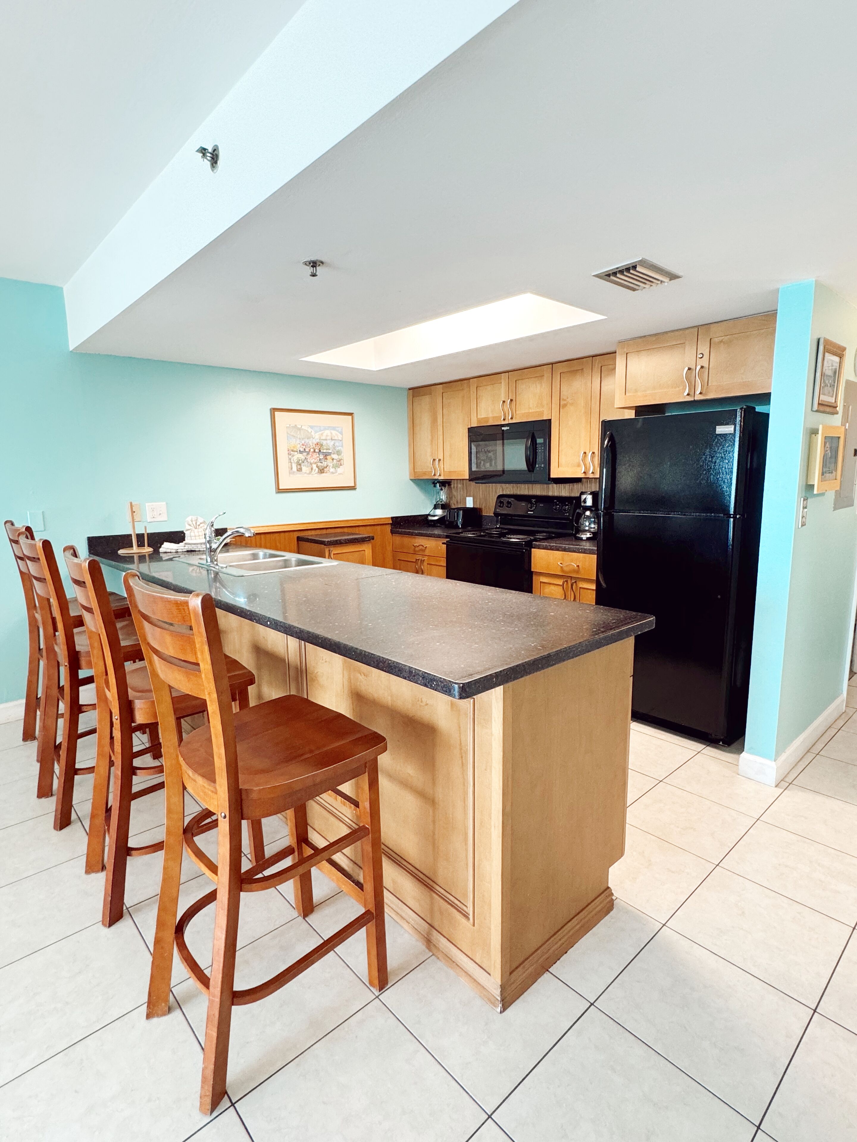 A modern kitchen with a central island, wooden bar stools, and a black refrigerator.
