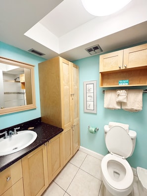 A bathroom with a skylight, wooden cabinets, a sink, a toilet, and a framed picture on the wall.
