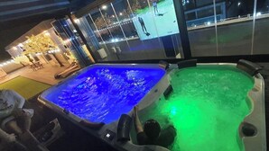 To boblebad med vand oplyst i blå og grønne farver, en pool med glas og lys, samt udsigt til en gade om natten.