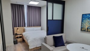 Et hotelværelse med seng, sofa, et lille bord, et billede og et vindue med gardiner.
