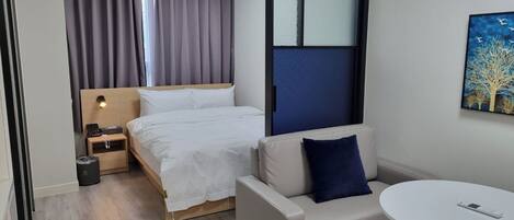 A hotel room with a bed, a sofa, a small table, a painting, and a window with curtains.