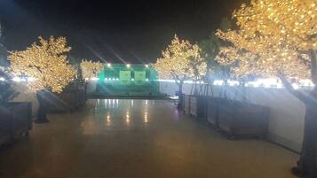 A corridor with trees adorned with lights, leading to a green-lit area with two doors.