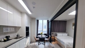 Et moderne hotelværelse med tekøkken, spiseområde med bord og stole samt en stor seng med sengegavl.