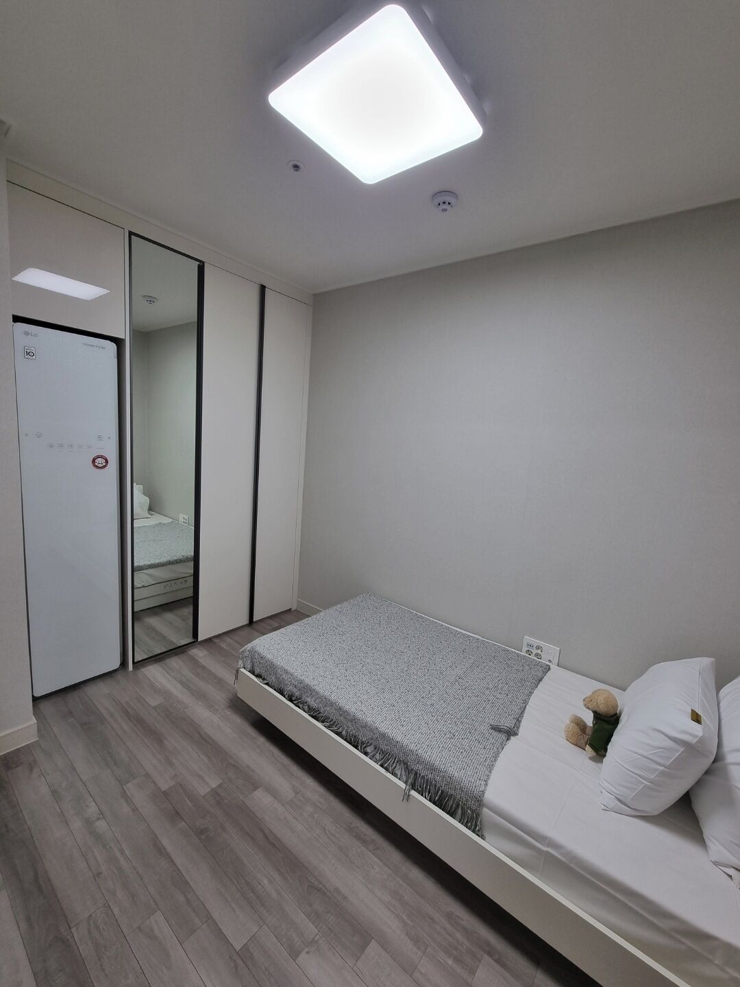 A modern bedroom with a bed, a wardrobe, and a ceiling light.
