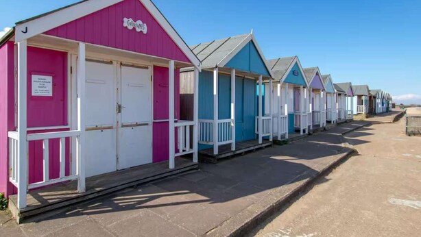 Une rangée de cabanes de plage, dont la cabane rose porte une pancarte sur laquelle on peut lire « Goosebumps ».