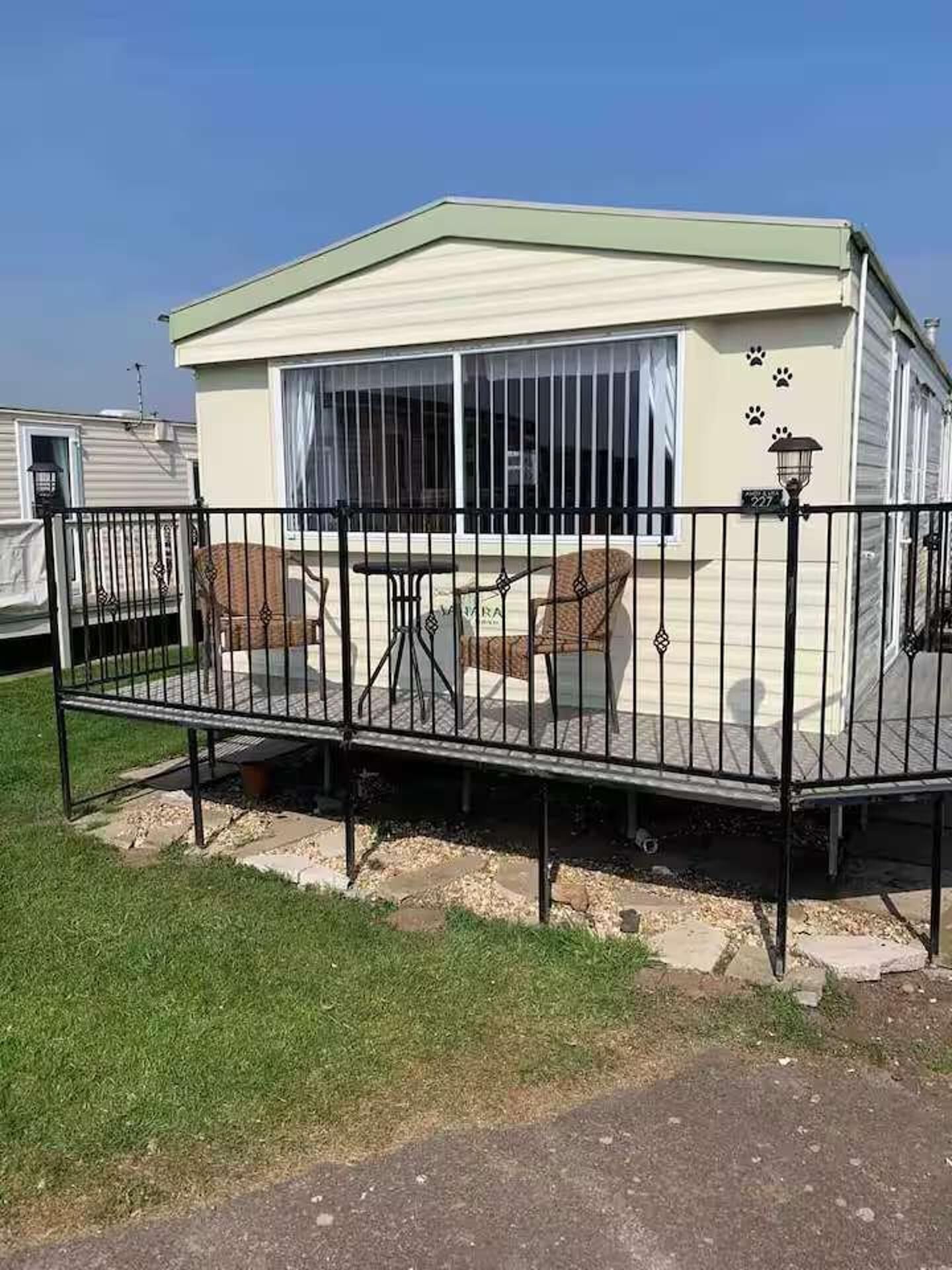 A mobile home with a fenced patio area, a small table, and a chair.