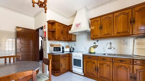 A kitchen with wooden cabinets, a stove, a microwave, and a dining area with a table and chairs. - New Sunset Haven in Gale-2br With Big Terrace (Albufeira)