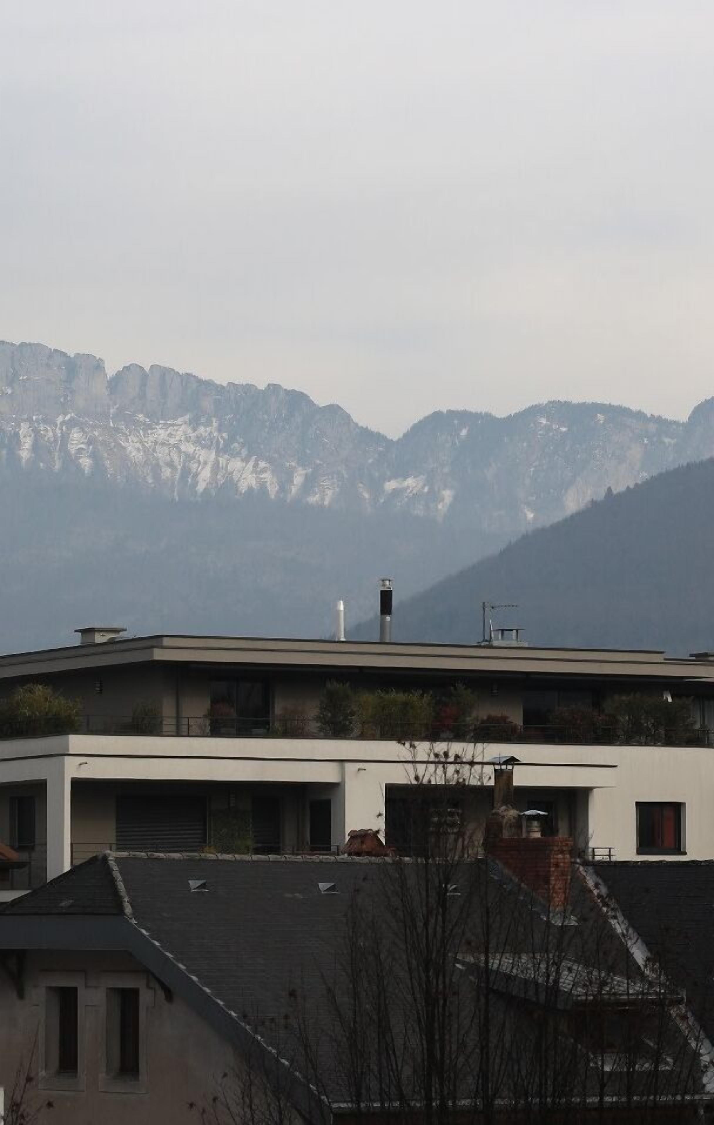 A modern building with a flat roof and a chimney, surrounded by mountains.