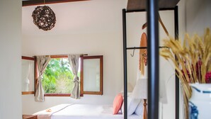 Un dormitorio con cama, ventana con cortinas, lámpara colgante y un jarrón con plantas secas.