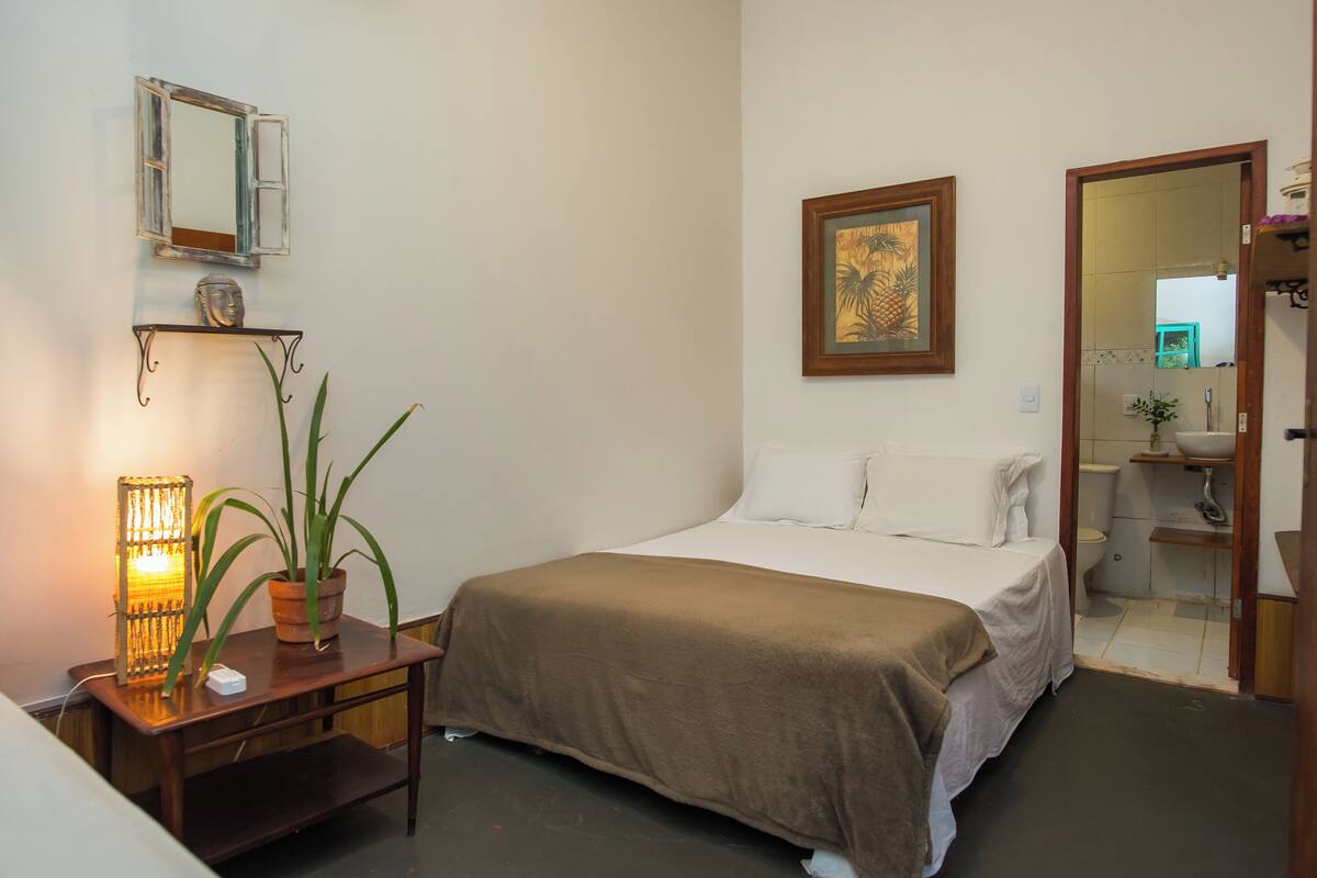Une chambre à coucher avec un lit, une table de chevet, une lampe, une plante en pot et un tableau encadré au mur.