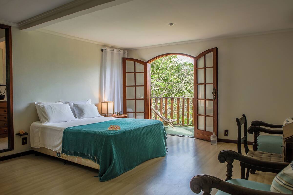Une chambre à coucher comprenant un lit, une table de chevet, une chaise et un balcon avec vue sur les arbres.
