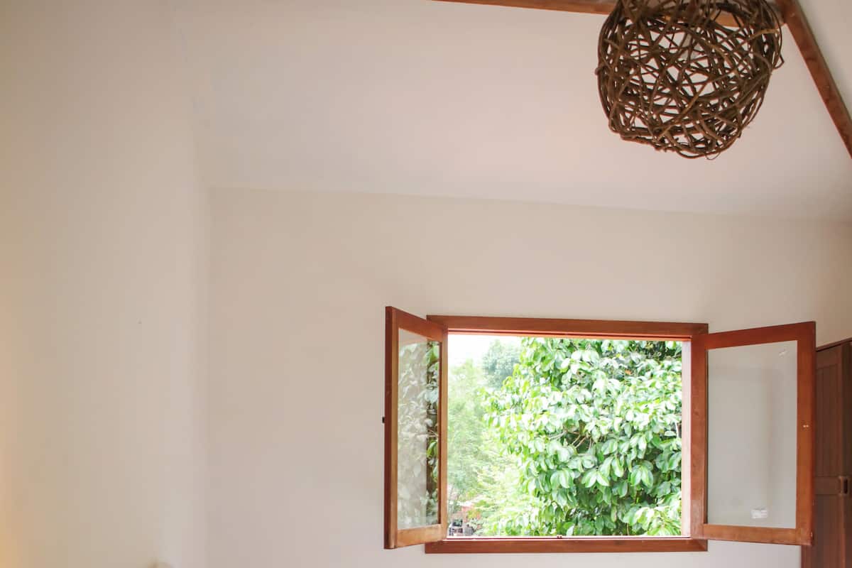 Une chambre à coucher avec un lit, une fenêtre, une poutre en bois au plafond et un luminaire suspendu.