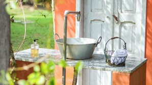 Un lavamanos rústico al aire libre con un lavabo de metal y grifo, un dispensador de jabón y un cubo metálico sobre un borde de hormigón.