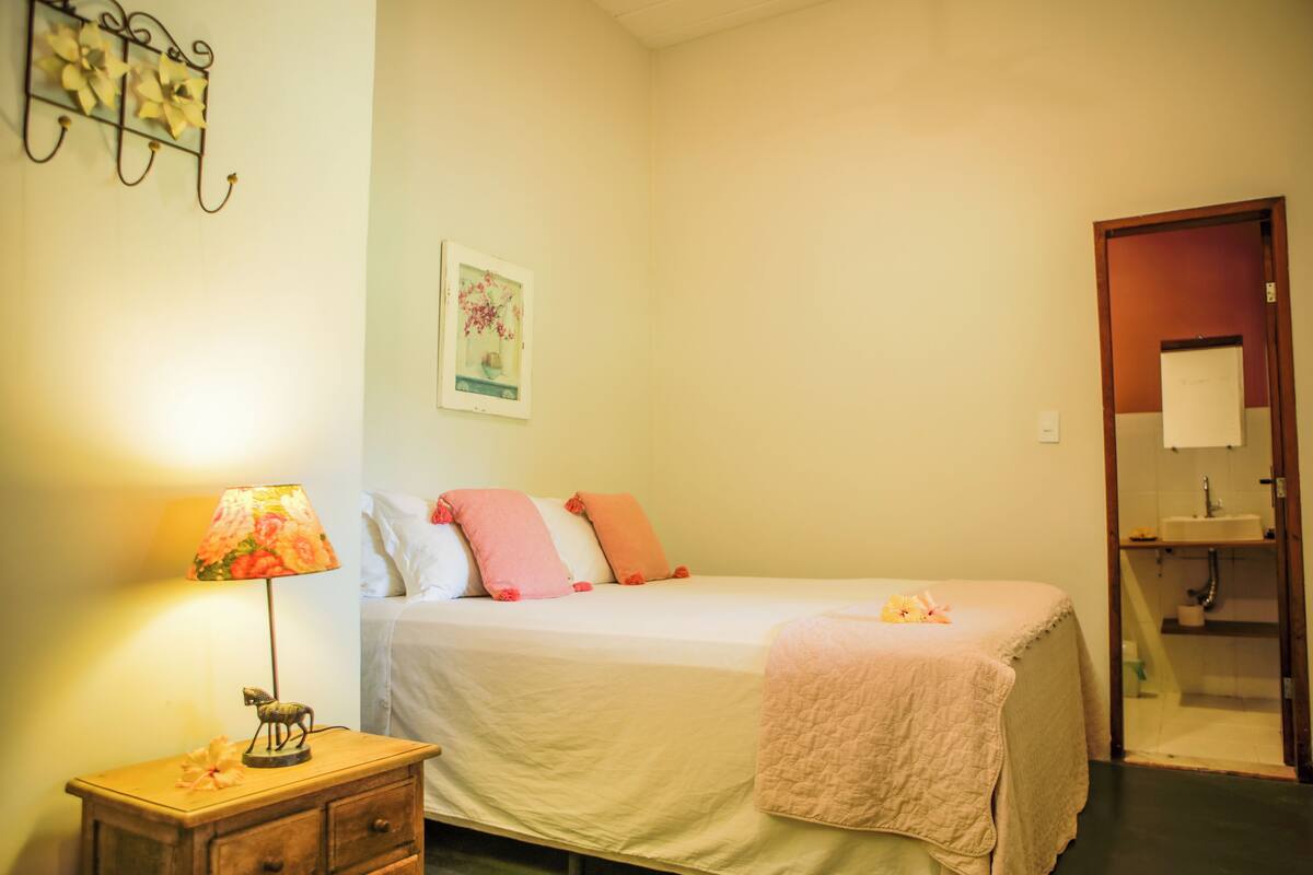 Une chambre à coucher avec un lit, une table de chevet avec une lampe, un tableau au mur et une porte de salle de bain.