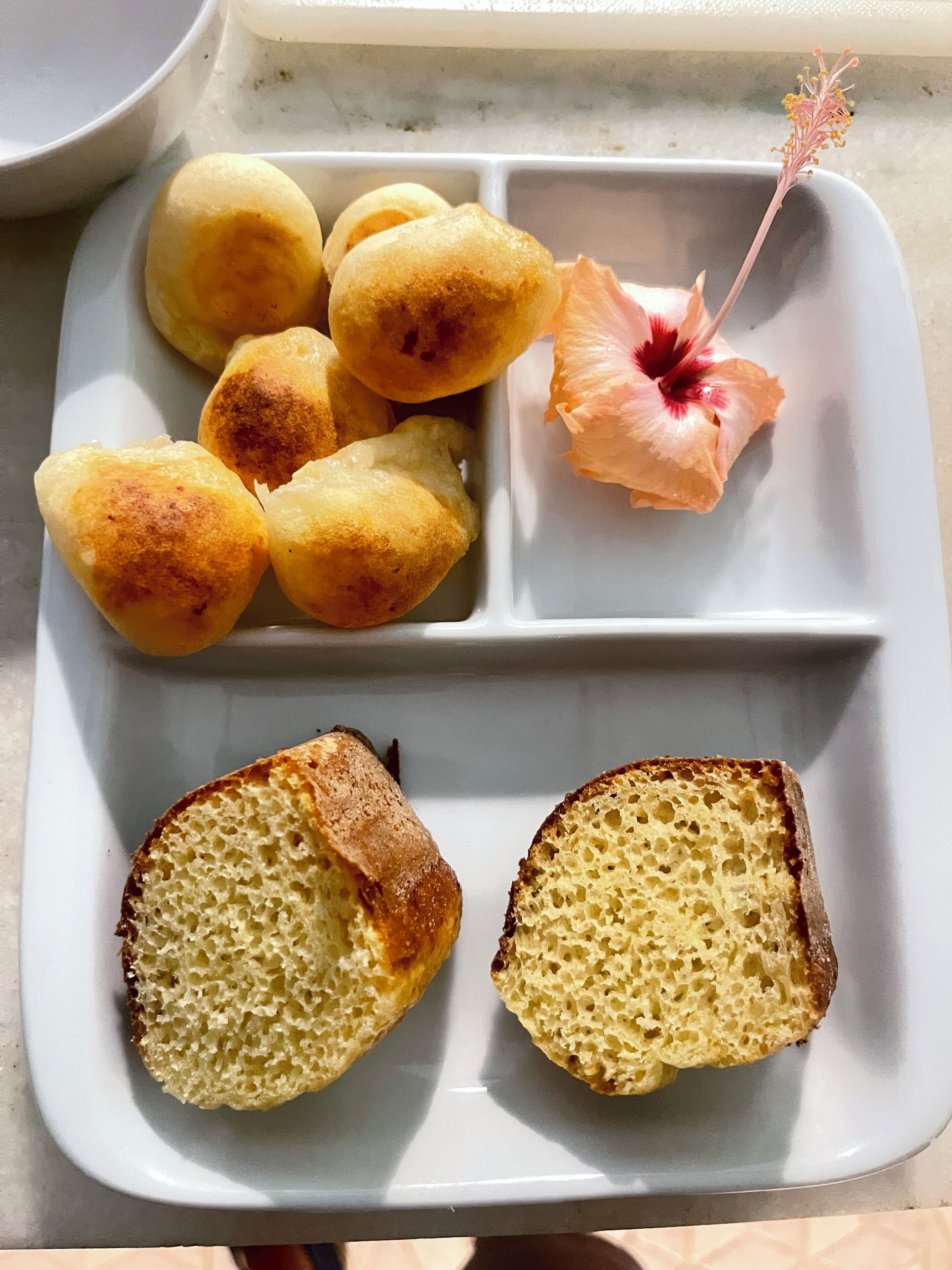 A white plate with three pieces of bread, one of which is cut in half, and a pink flower with a yellow center.