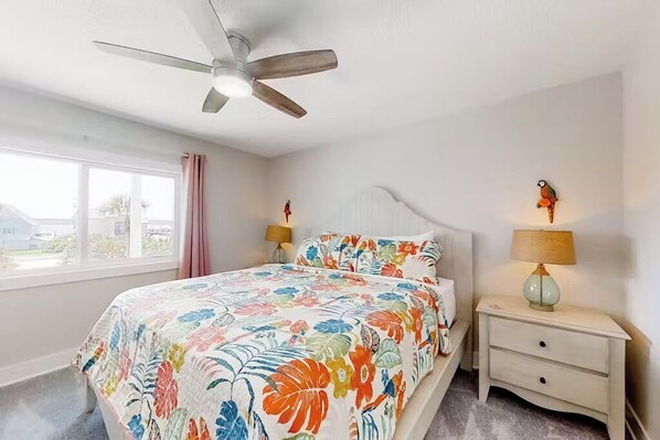 A bedroom with a bed, a ceiling fan, two bedside lamps, a nightstand, a window with curtains, and a view of the outside.